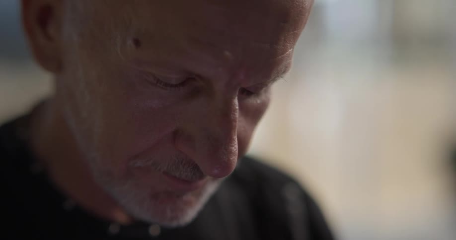An elderly man looks down with his eyes closed