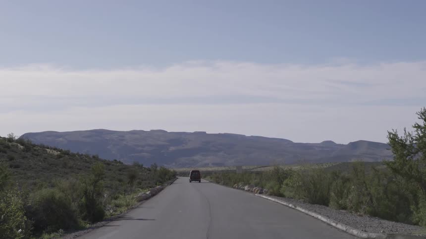 Van drives along road through hill during the day