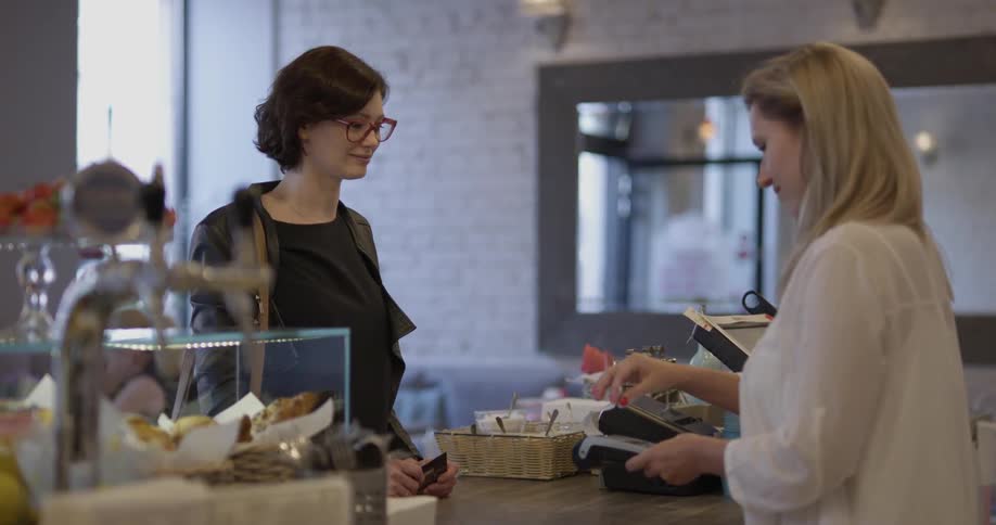 A woman working at a cafe gives a receipt to a customer