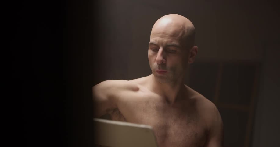 A man with no shirt on looking at a laptop