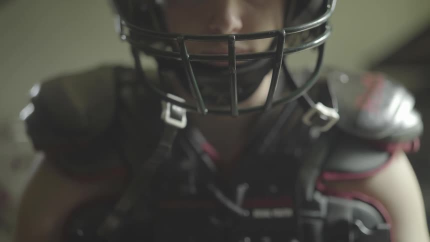 A youngster is wearing football pads and a football helmet