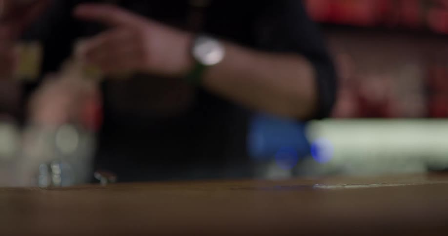 Bartender picks up four shot glasses filled with liquid and walks away