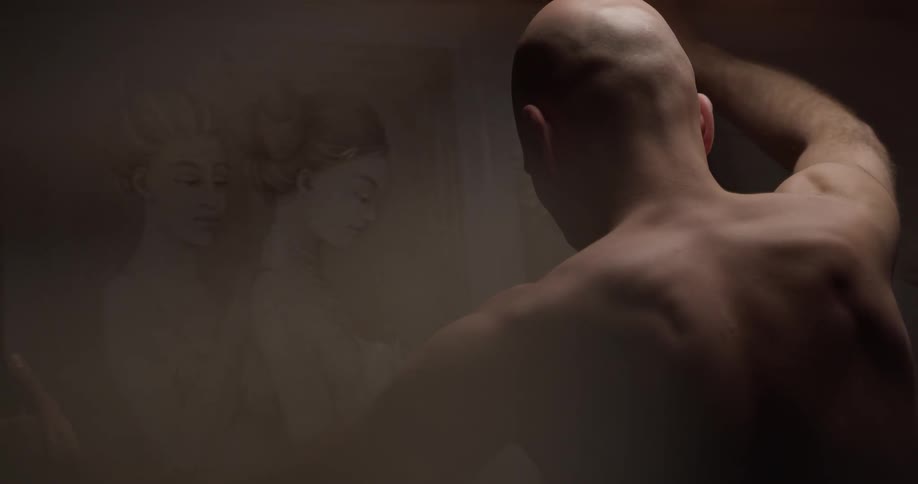 A shirtless man is looking at a drawing
