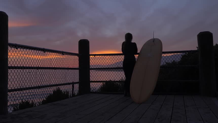 A woman stands on a deck while looking out over the ocean at dusk