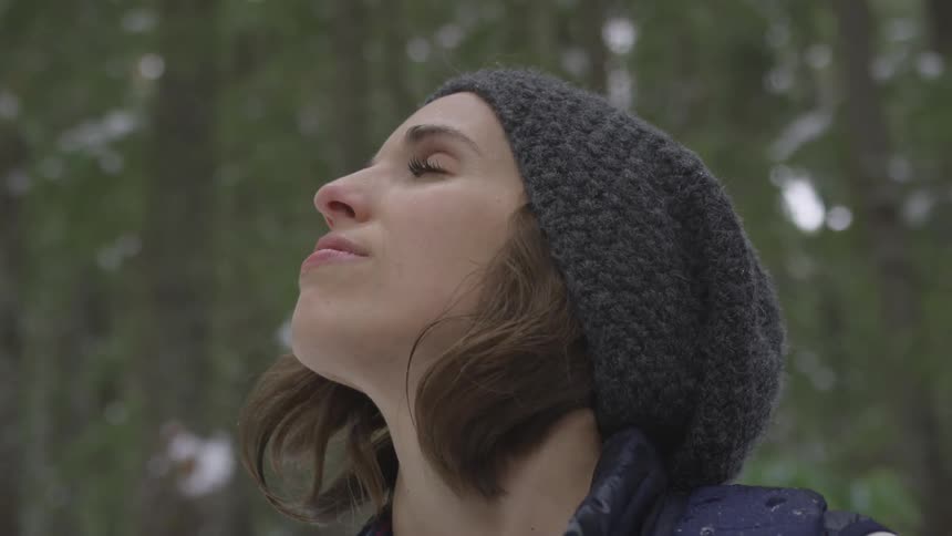 A woman raises her face toward the sky outside in the snow
