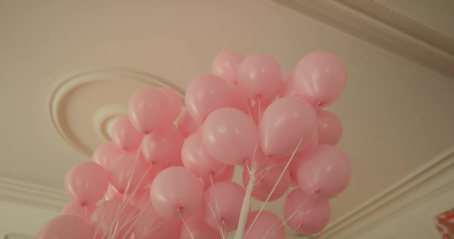 Woman carrying huge bouquet of pink balloons through house