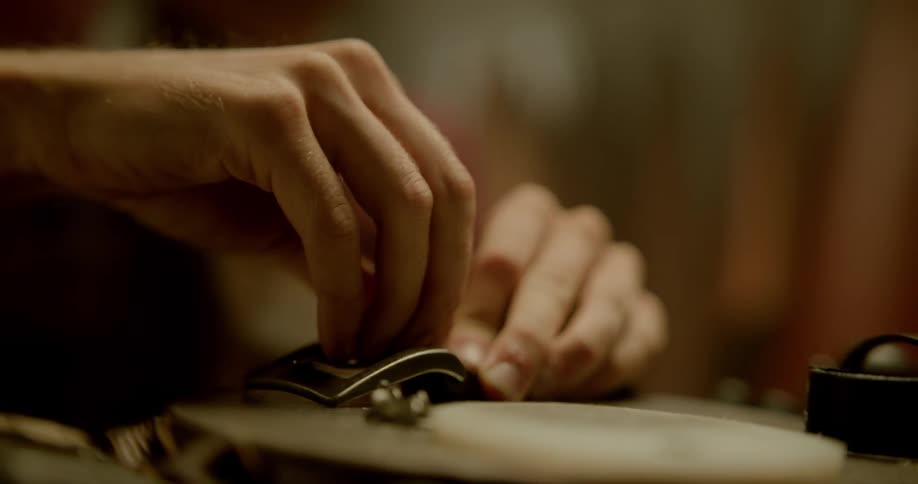 A man uses a nail to punch holes into a belt