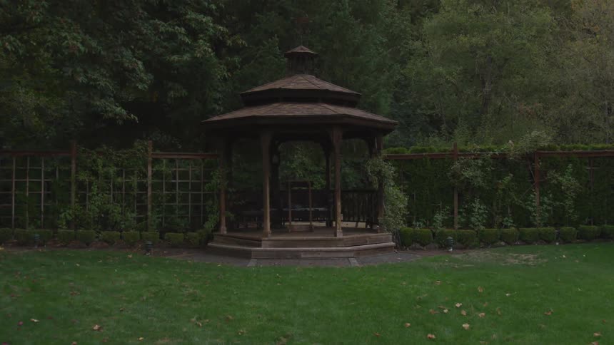 Gazebo in backyard before trellised fence and formal bushes
