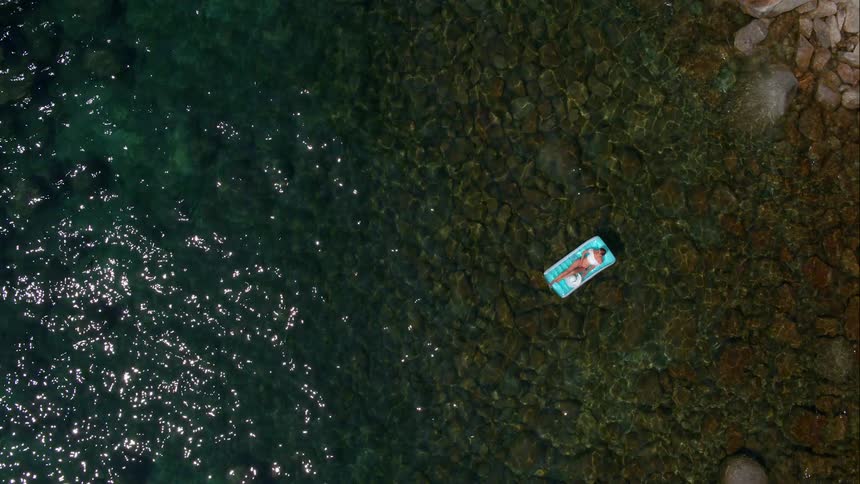 A woman is floating on the water above rocks