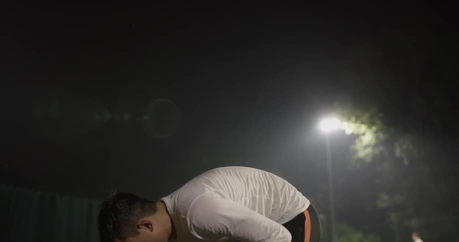 A sweaty man grabs an article of clothing from the ground and throws it over his shoulder