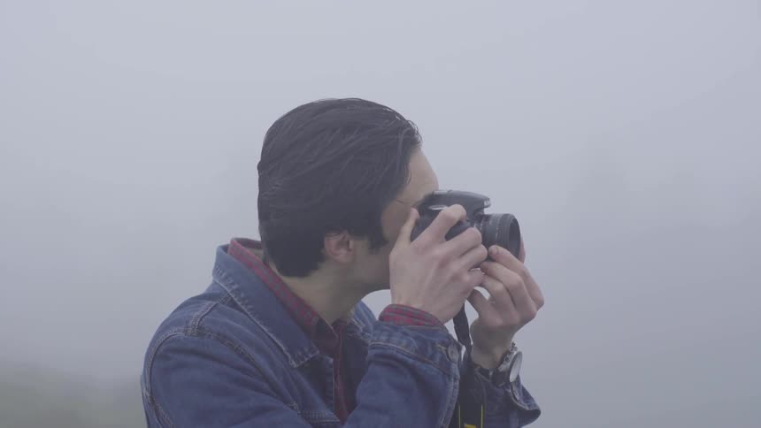 Man standing in fog lifts camera and takes picture