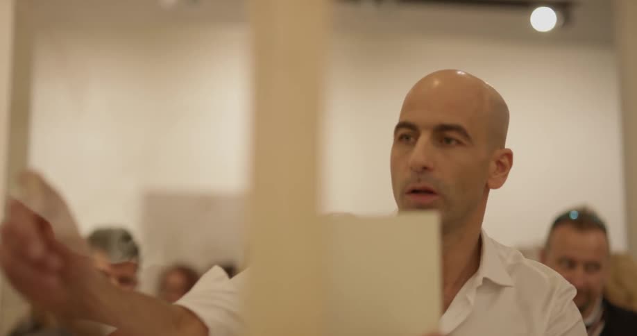 An artist drawing on a clear glass panel in a crowded studio