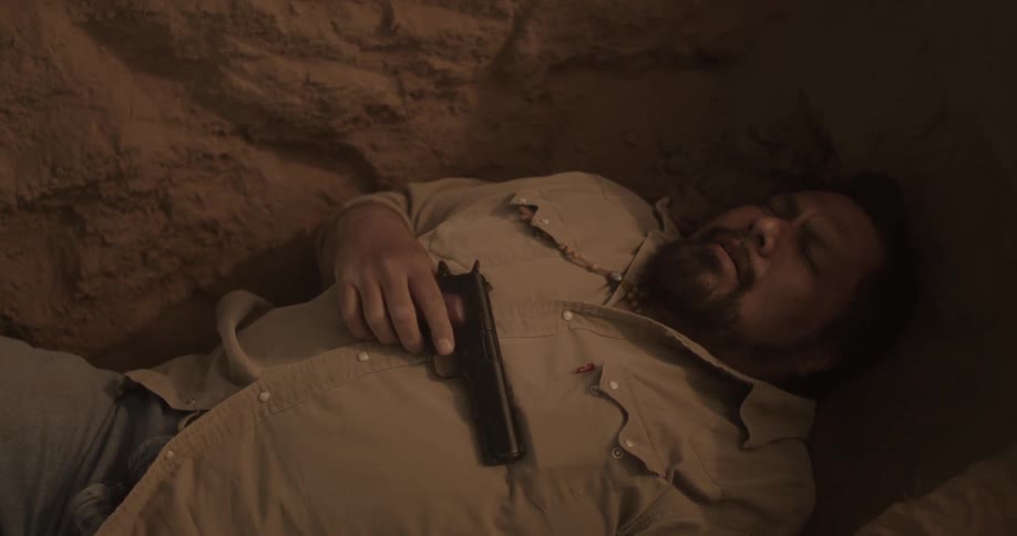 A man pulls a gun out of his pocket while he lies in a hole
