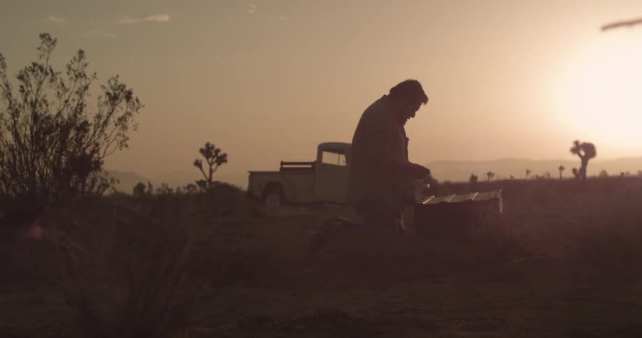 A man looking in a chest in the desert at sunset