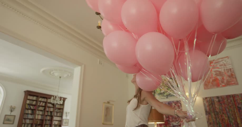 A woman is putting balloons on the ceiling