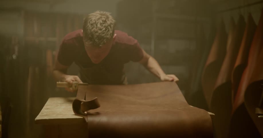 A man in a workshop cutting a piece off of material