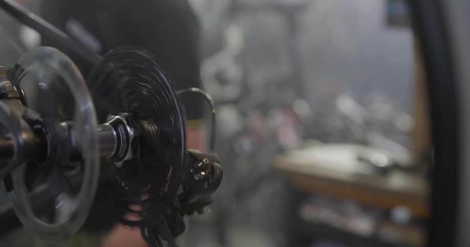 A man petals a bicycle wheel with his hands at the bike repair shop indoors in a well lit room