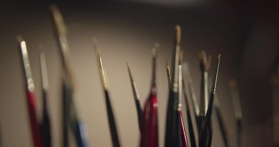 Blurry body approaches the foreground and comes into focus then grabs one of the paint brushes and walks away