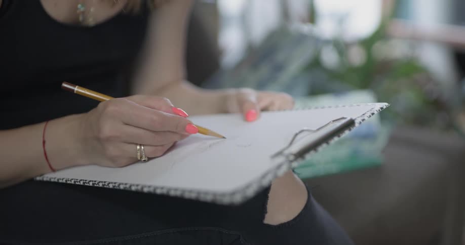 A woman draws on a sheet of white paper on a clipboard with a pencil
