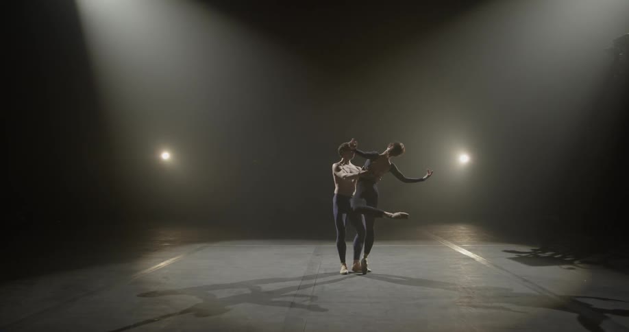 Two dancers slowly pirouette on a stage