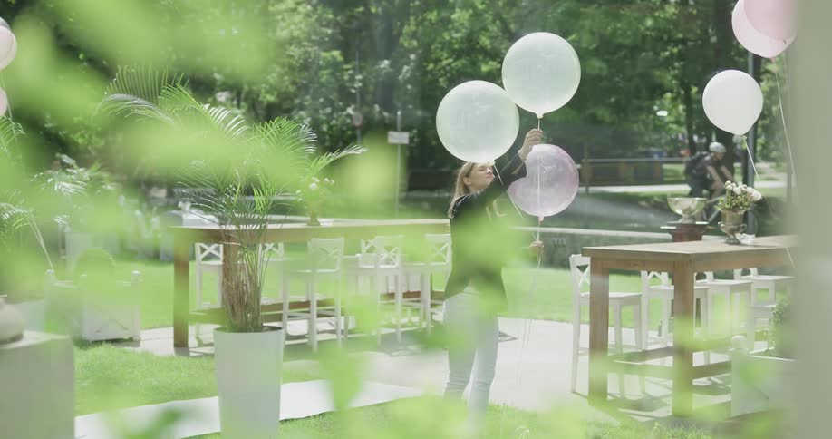 Woman pulls balloons down that are attached to a table