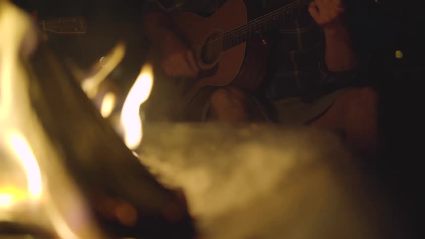 Man plays guitar near bonfire at night