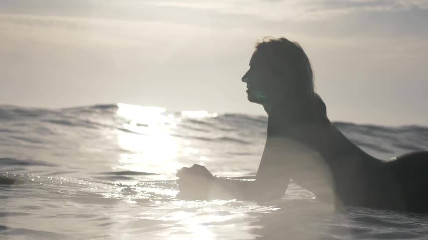 A woman lays on a surfboard in the middle of the ocean