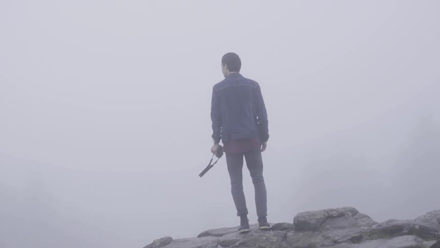Man carrying a camera looks out at foggy landscape
