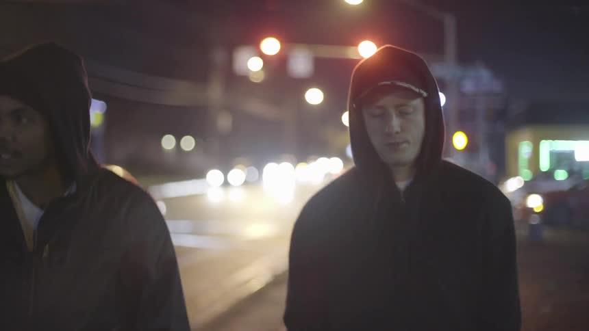 Two young men walking down the street at night with their hoods up and hands in their front pockets