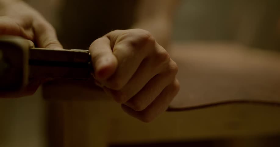 Man cuts strip of leather off a larger piece