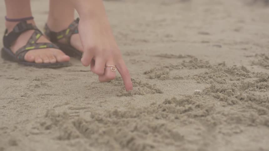 A person draws in the sand with their finger