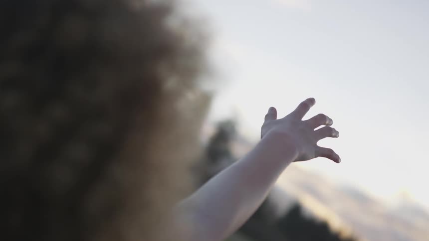 A person reaches out their arm in a field at sunset