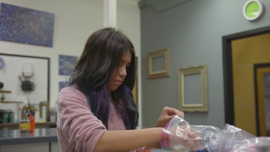 A girl in a classroom taking beads out of a ziploc bag