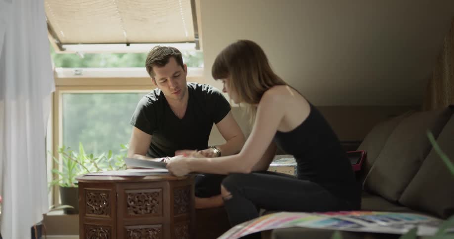 A woman and man are sitting on the bed writing on paper