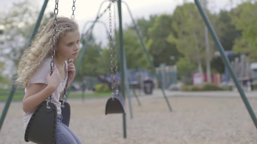 Girl with long curly blonde hair sits on swing