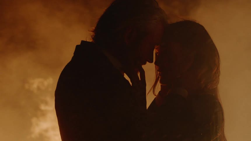 A man and woman touch each other's faces while standing in front of a fire