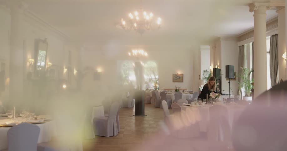 Woman walks across formal dining area and adjusts floral arrangement on table