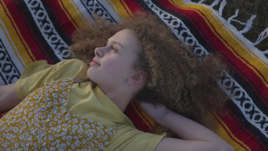 A little girl lays on her back on a blanket