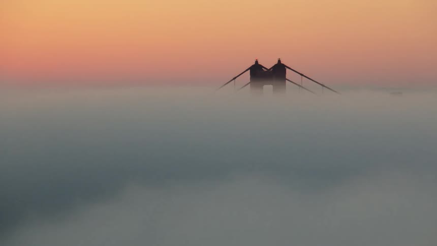 Fog floats in front of a bridge at sunset