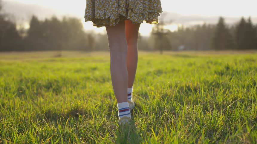Bottom half of a girl walking through a field on a sunny afternoon