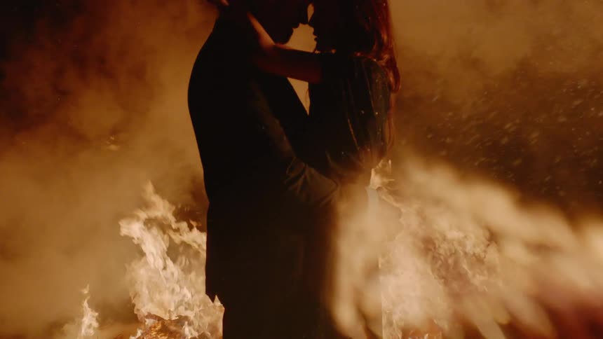 Man and woman kissing in front of a fire