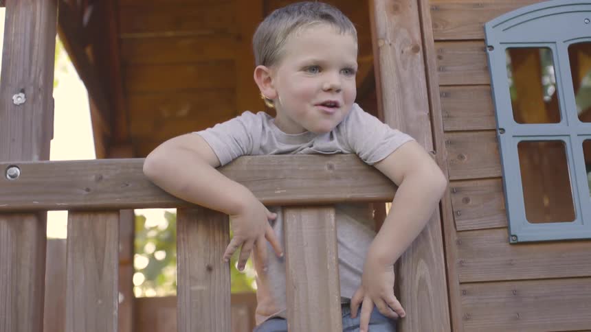 A young boy plays outside in a playhouse