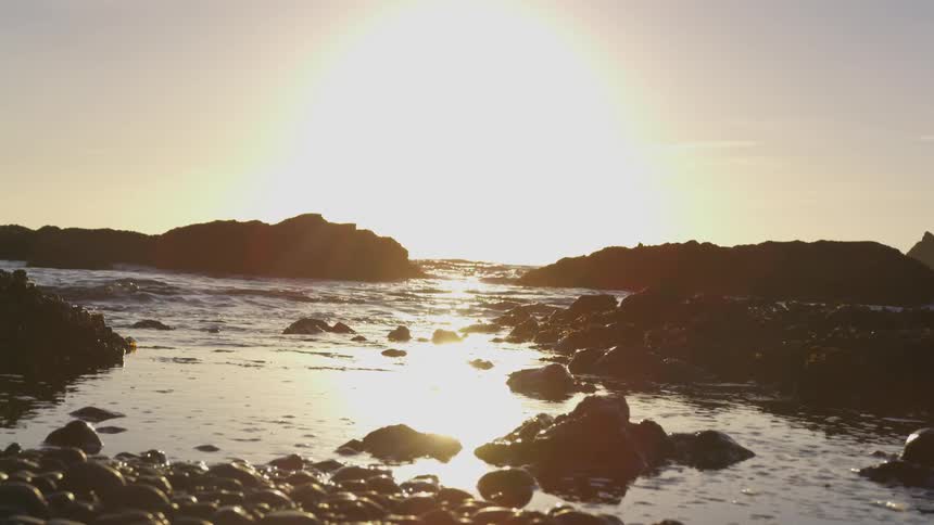 Water swirls around rocky outcroppings at beech under setting sun