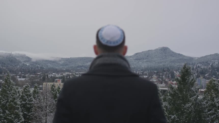 Man wearing a yamaka looking over a snowy town