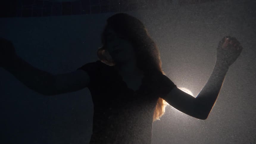 Woman swims underwater with light behind her