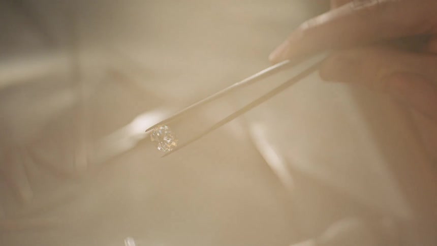 A person holds a small diamond with tweezers indoors