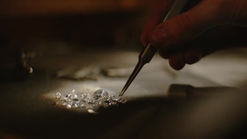 A person is picking up diamonds with a tweezer