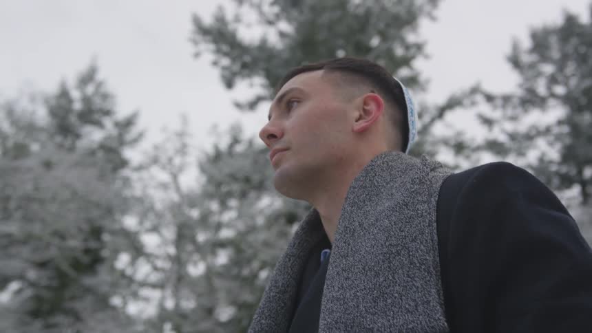 A man is walking outside near a forest covered in snow