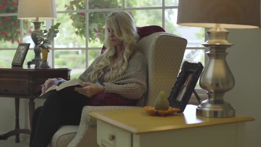 A woman sits in a living room chair and reads a book