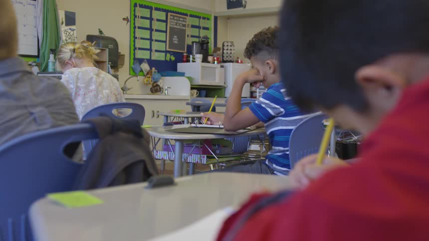 Children sit at their desks writing with pencils in class